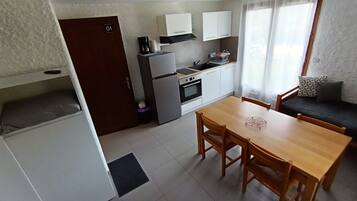 Eine kleine Küche mit Kühlschrank, Herd und Mikrowelle. Es gibt einen Esstisch mit Stühlen und eine Couch mit Kissen.