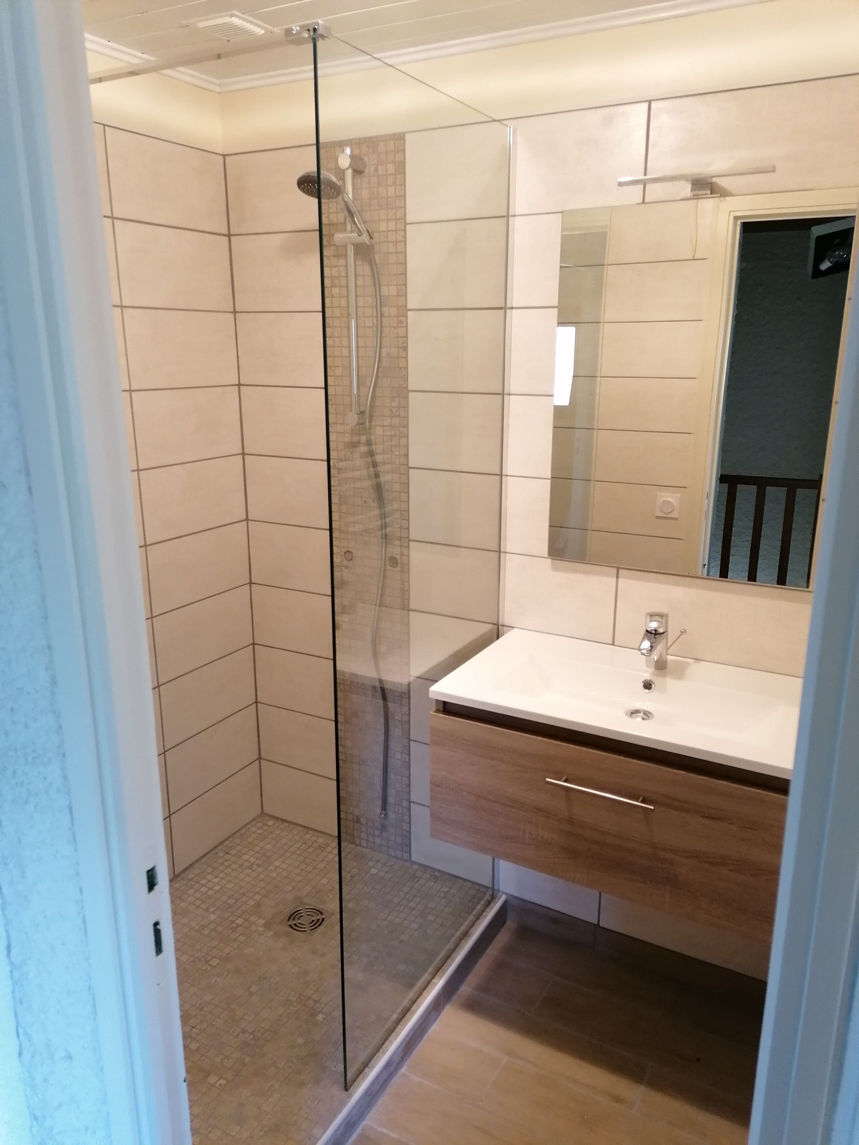 A modern bathroom with a glass-enclosed shower, a white sink, and a wooden vanity.
