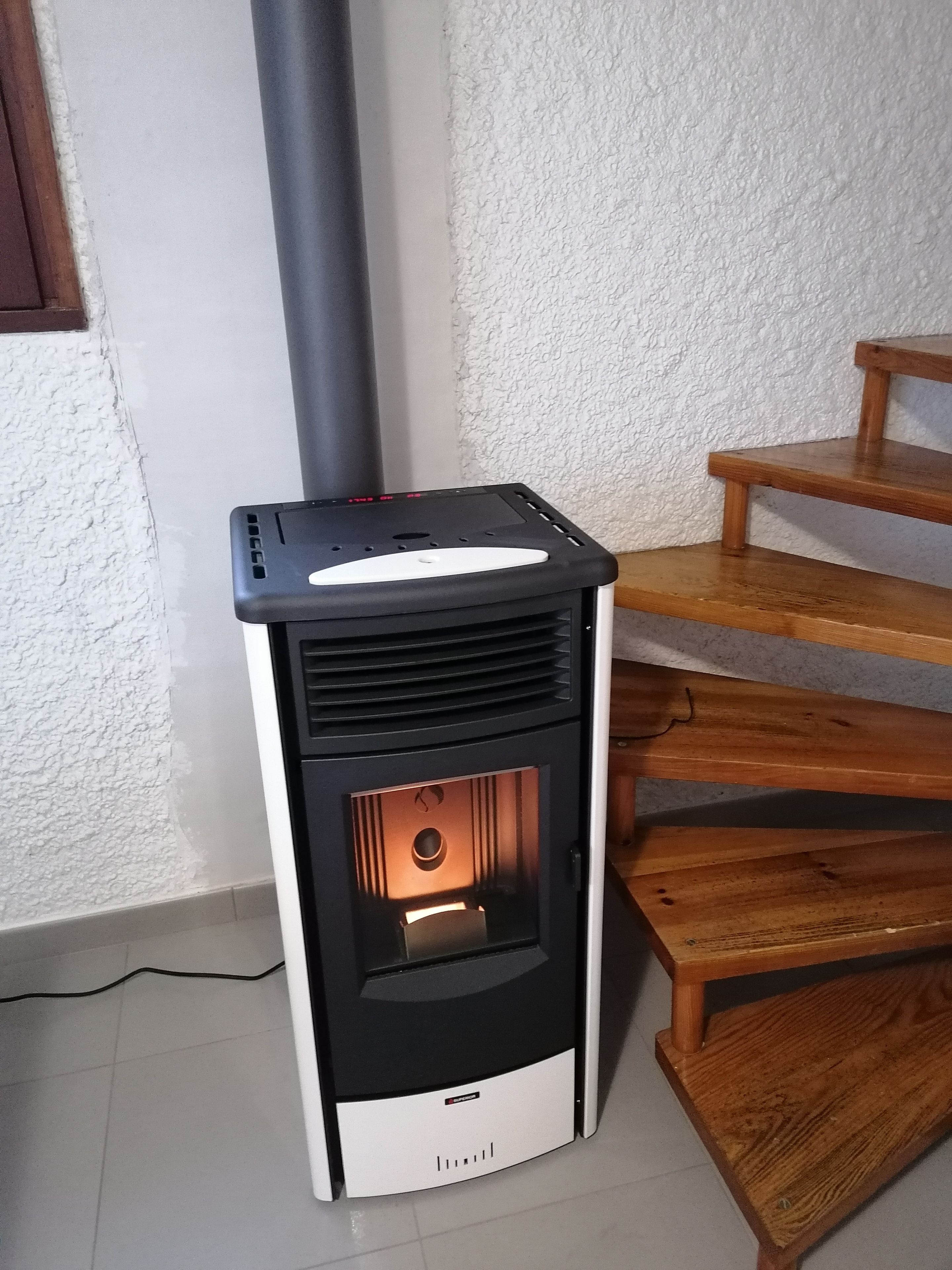 Una estufa de leña con panel de control digital, ubicada junto a una escalera de madera.