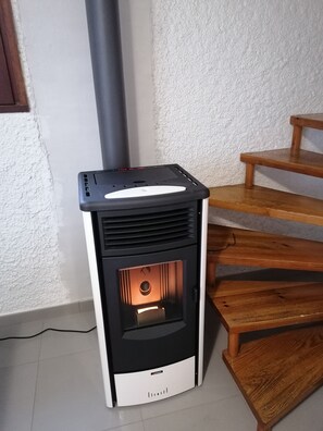 Una estufa de leña con panel de control digital, ubicada junto a una escalera de madera.