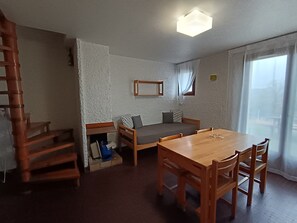 Una habitación con una mesa de comedor de madera, un sofá, una escalera y una ventana con cortinas.