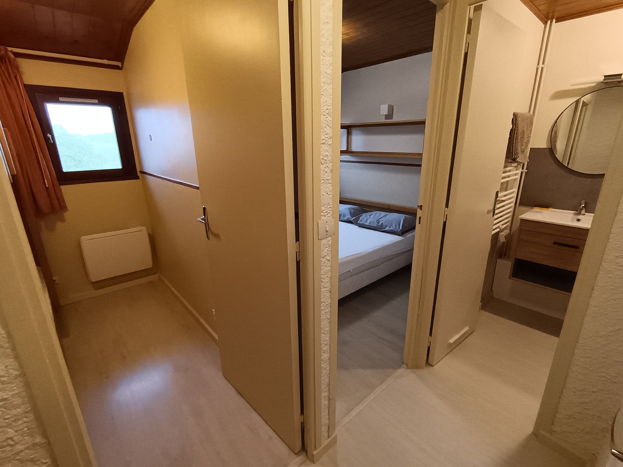 Ein schmaler Flur führt zu einem Schlafzimmer mit Etagenbett, kleinem Fenster und einem Badezimmer mit Spiegel und Waschbecken.