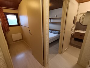 A narrow hallway leading to a bedroom with a bunk bed, a small window, and a bathroom with a mirror and sink.