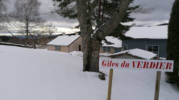 En skylt med texten ”Gîtes du VERDIER” placerad i en lantlig miljö med snötäckt mark och hus i bakgrunden.