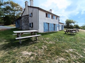 A two-story building with a stone facade and blue shutters, surrounded by a grassy lawn with picnic tables.