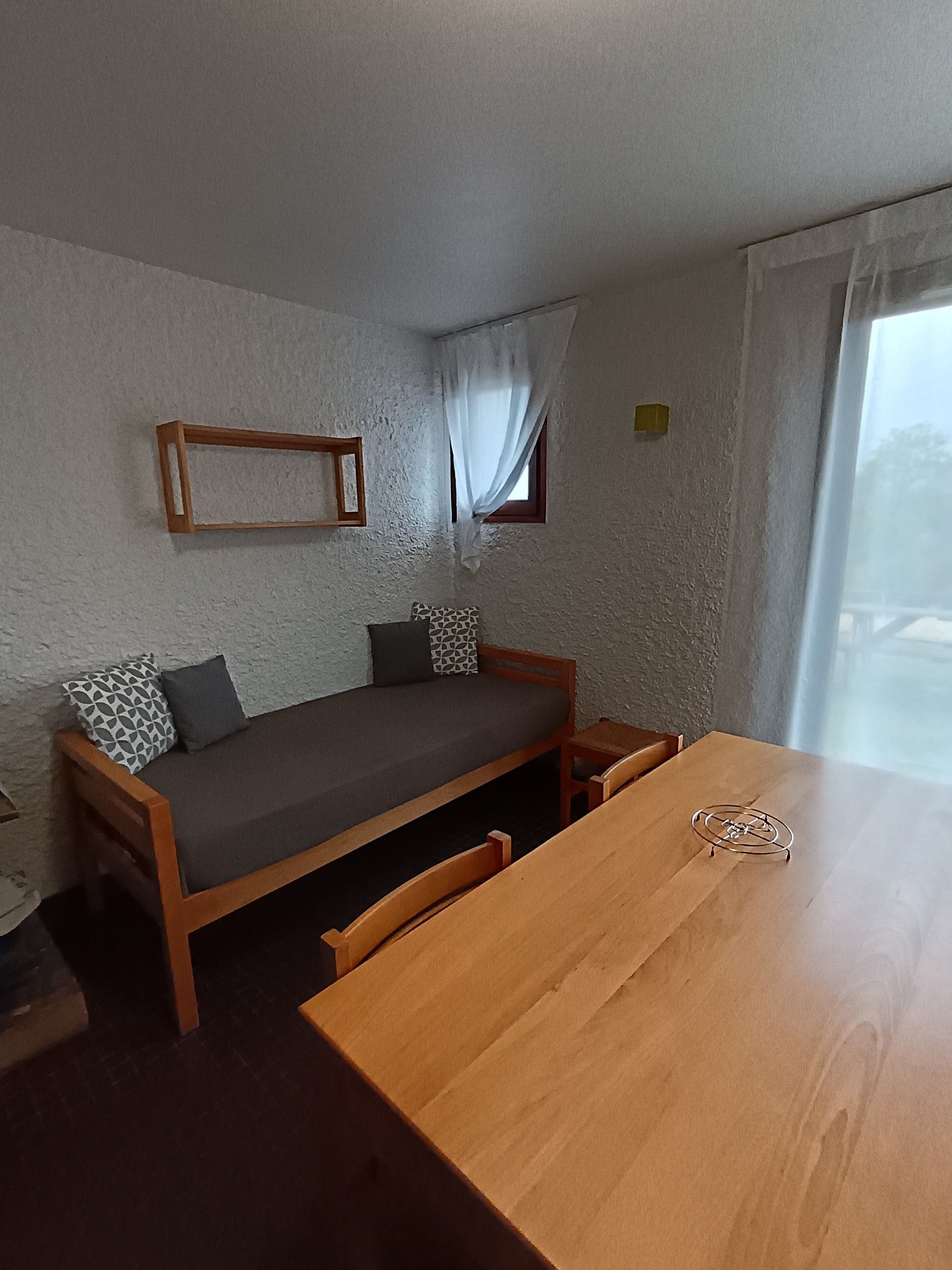 A compact room with a wooden bed, a dining table, and a window with curtains.
