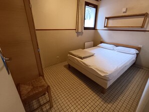 Una habitación pequeña con cama individual, cabecera de madera, mesita de noche y ventana con cortinas.