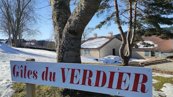 A sign with the text 'Gîtes du VERDIER' in a rural setting with snow-covered ground and trees.