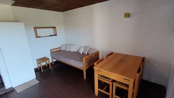 A room with a wooden bed, a small table, and a larger dining table.