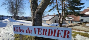 Un cartel con el texto 'Gîtes du VERDIER' en un entorno rural con suelo cubierto de nieve y árboles.