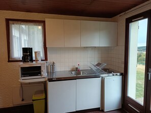 Una cocina compacta con armarios blancos, horno integrado, cafetera y lavamanos.