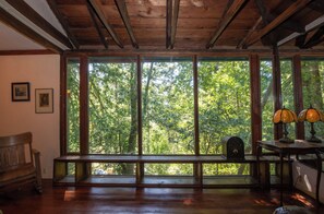 Ein Zimmer mit großem Fenster, Holzbalken, einer Bank, einem Tisch mit Lampen und gerahmten Bildern an der Wand.