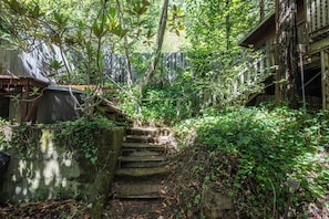 Eine steinerne Treppe führt zu einer hölzernen Struktur, umgeben von dichtem Grün.