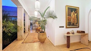 A hallway with a large potted plant, a painting, and a small table with books and decorative items. - ZALUNA Marrakech Private Villa & Heated Pool (Sidi Bouzguia)