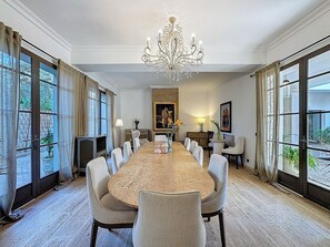 A spacious dining room with a long table, multiple chairs, a chandelier, and large windows with curtains. - ZALUNA Marrakech Private Villa & Heated Pool (Sidi Bouzguia)