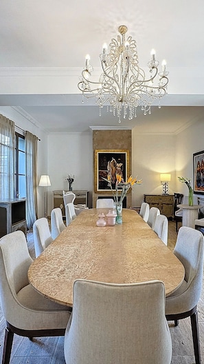 A dining room with a large oval table, multiple chairs, a chandelier, a painting on the wall, and a window with curtains. - ZALUNA Marrakech Private Villa & Heated Pool (Sidi Bouzguia)