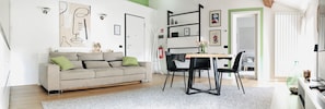 Ein modernes Wohnzimmer mit einer Couch, einem Esstisch mit Stühlen und einer Küchenzeile mit Kühlschrank und Schränken.