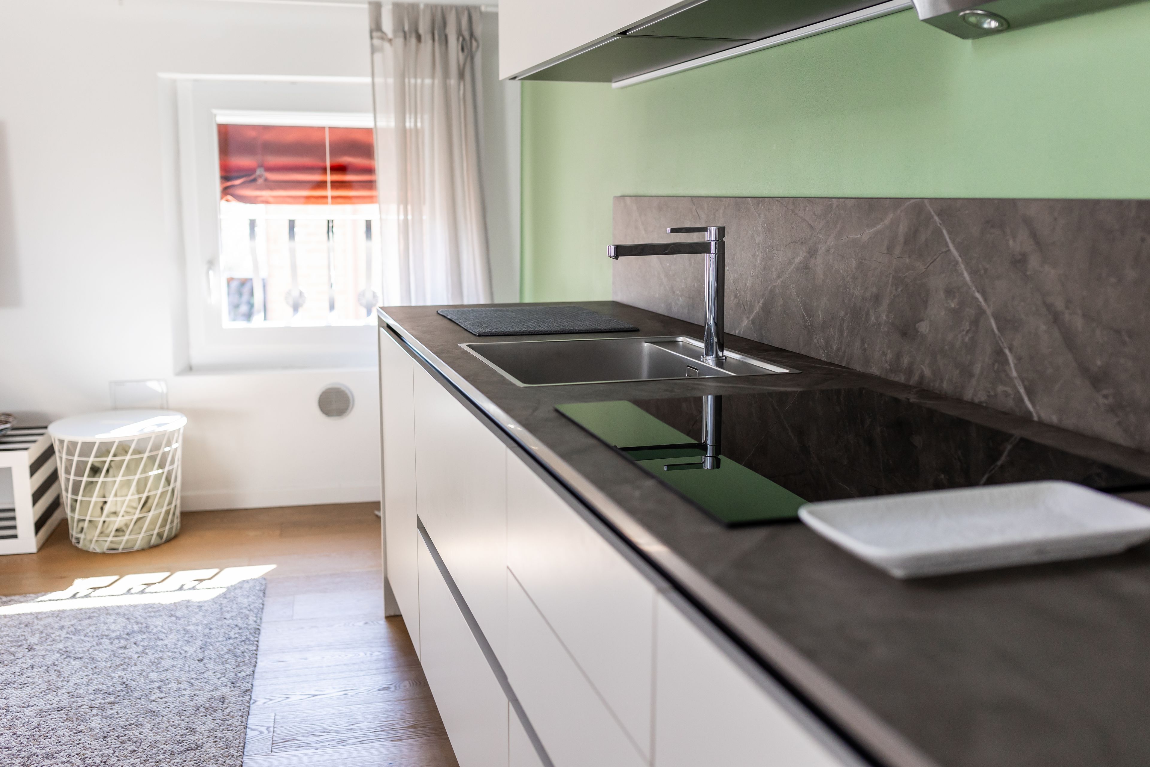 A modern kitchen with a black countertop, a stainless steel sink, and a green backsplash.