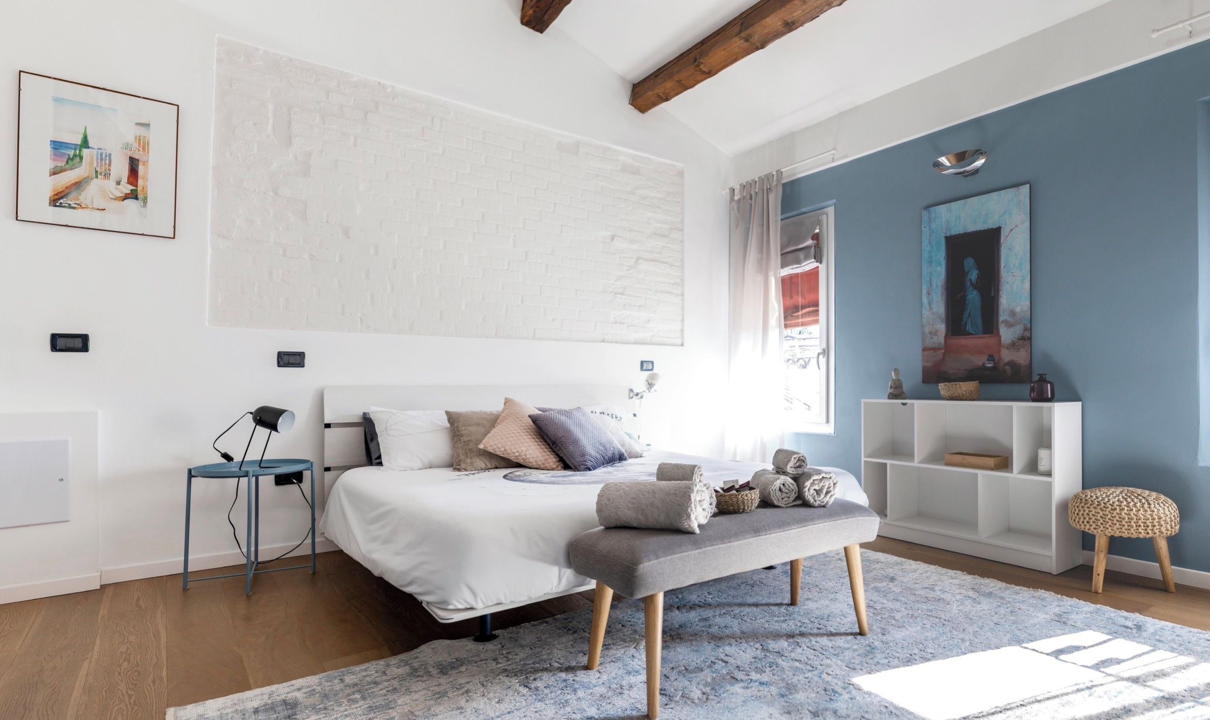 Quarto moderno com cama grande, mesas de cabeceira, um banco e vista para o exterior.