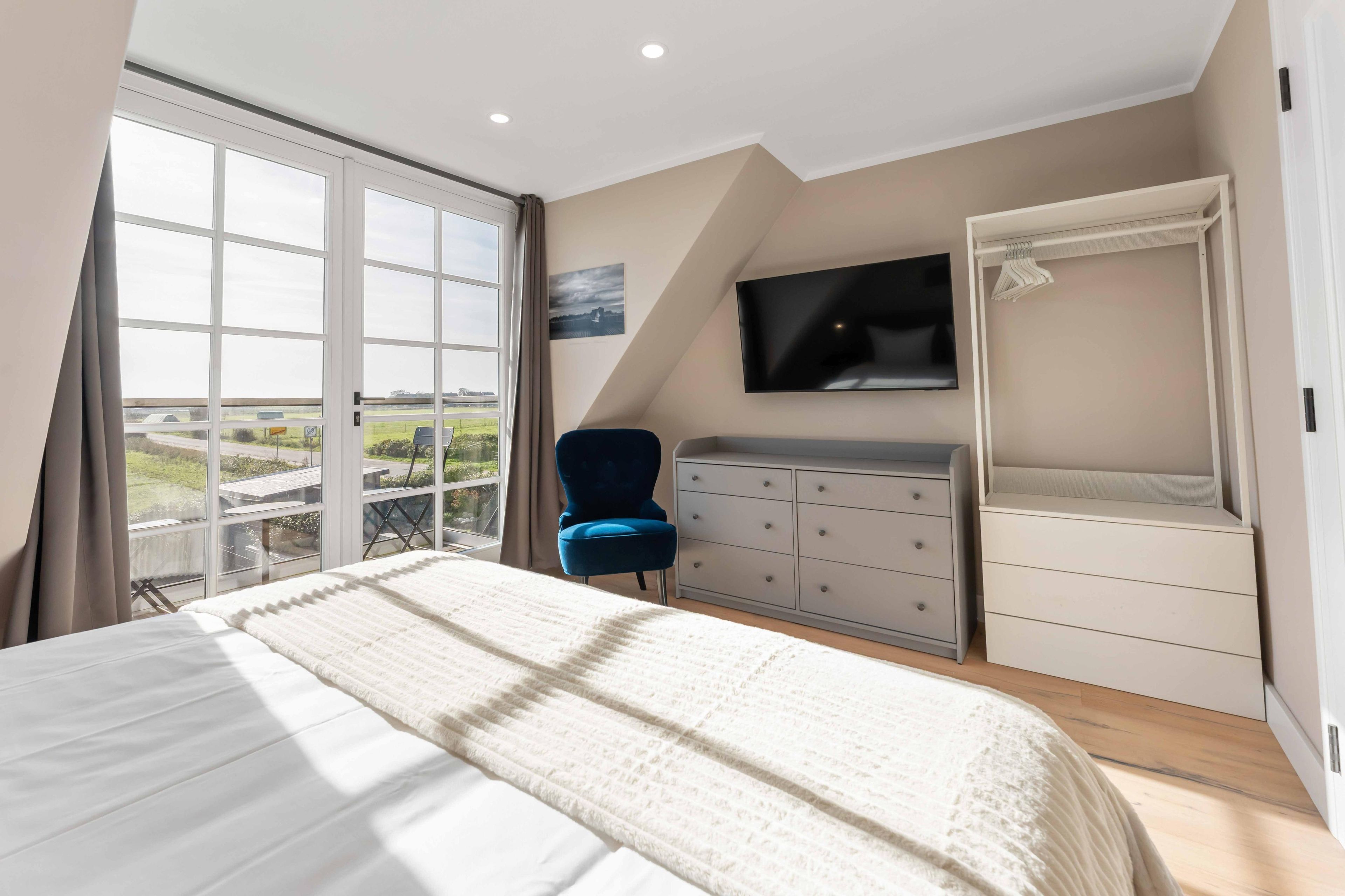 Een slaapkamer met een groot bed, een kaptafel, een aan de muur bevestigde televisie en een raam met uitzicht op het landschap.