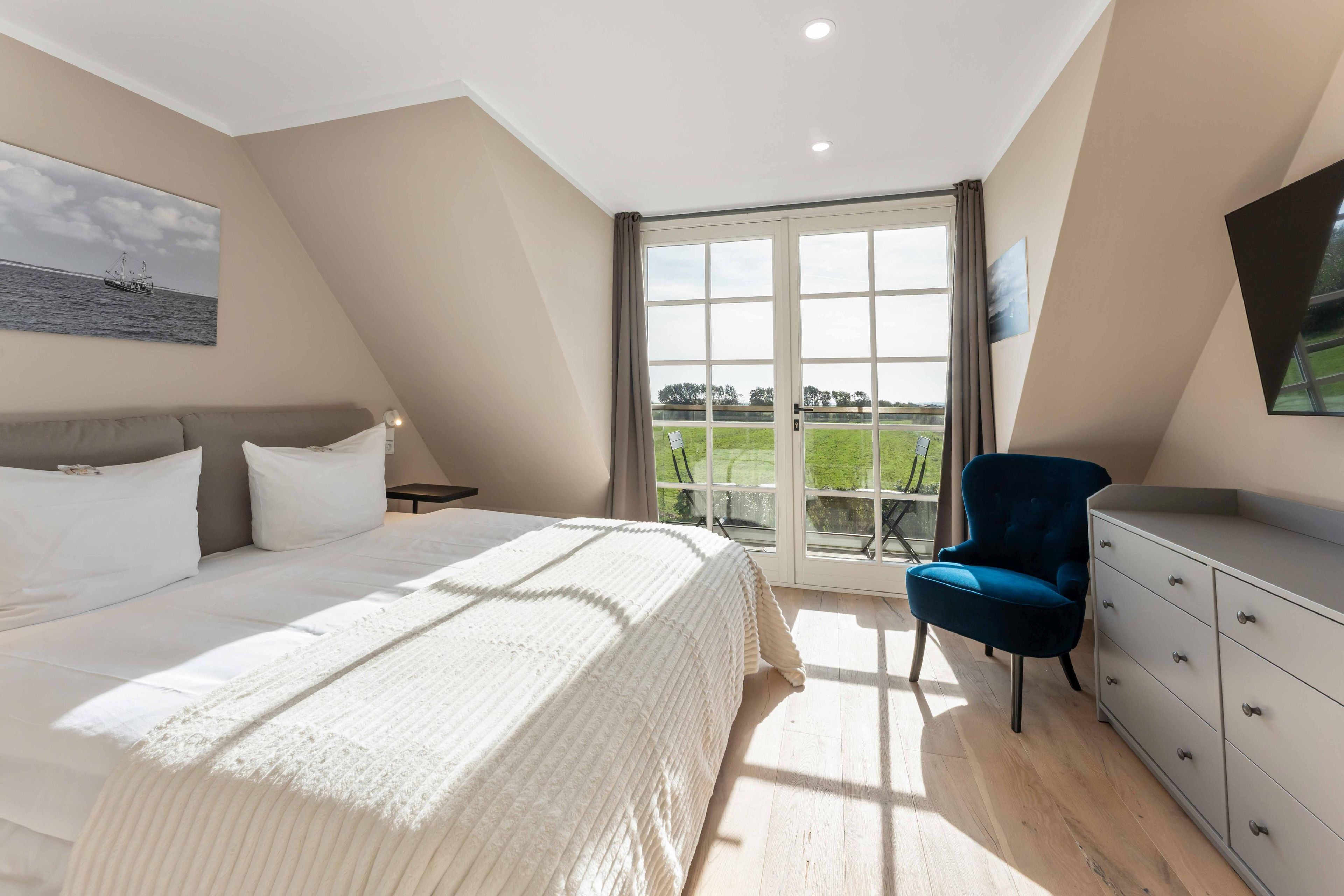 A bedroom with a bed, a chair, a dresser, and a large window with a view of the outdoors.