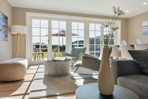 Un salon moderne avec une grande fenêtre, un canapé, un fauteuil, une lampe et un vase rempli de fleurs.