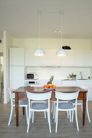 A modern kitchen with white cabinets, a wooden dining table, and two pendant lights. - Il Cascinale 3: Pool, Relaxation, Thermal Baths, Gardaland (Colà)