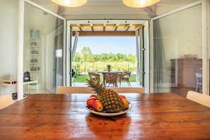 A dining table with a fruit bowl in the center, a glass door leading to an outdoor patio area with a view of a vineyard. - Il Cascinale 3: Pool, Relaxation, Thermal Baths, Gardaland (Colà)