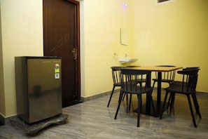 Una habitación pequeña con refrigerador, lavamanos y una mesa de comedor con sillas.