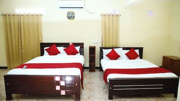 Habitación de hotel con dos camas, ventilador de techo, unidad de aire acondicionado y un reloj en la pared.