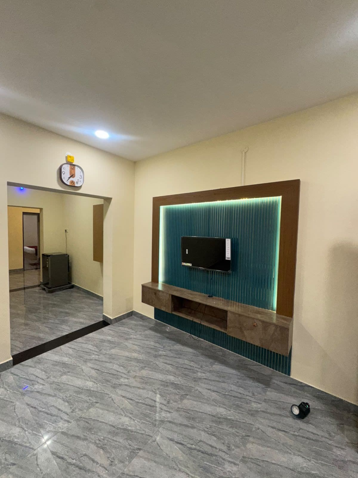 A modern room with a flat-screen TV mounted on a teal accent wall, a wooden console below, and a marble floor.