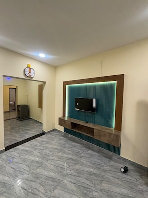 A modern room with a flat-screen TV mounted on a teal accent wall, a wooden console below, and a marble floor.