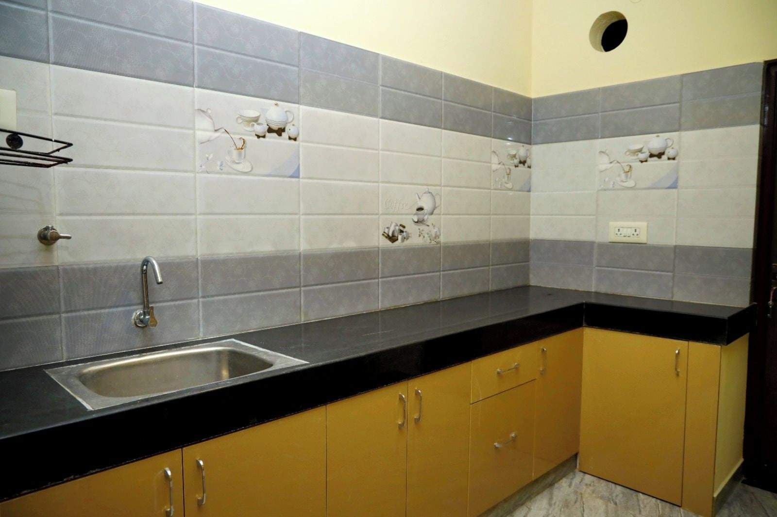 A kitchen with a black countertop, stainless steel sink, and yellow cabinets.