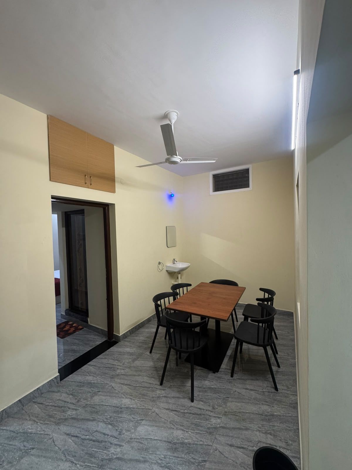 Ein Zimmer mit Esstisch, Stühlen, Deckenventilator, Spüle und einer Tür zu einem weiteren Raum.