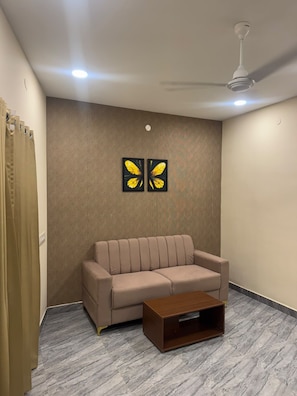 Una habitación con un sofá color beige, una mesa de centro de madera y dos piezas de arte mural con forma de mariposa.
