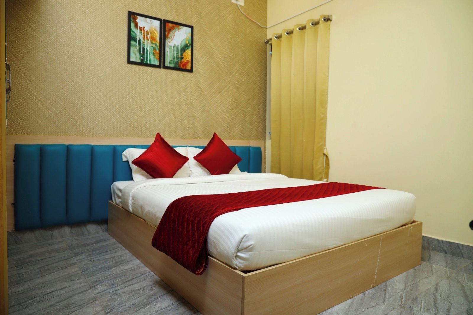 A hotel room with a bed, a headboard, a red throw blanket, and a painting on the wall.