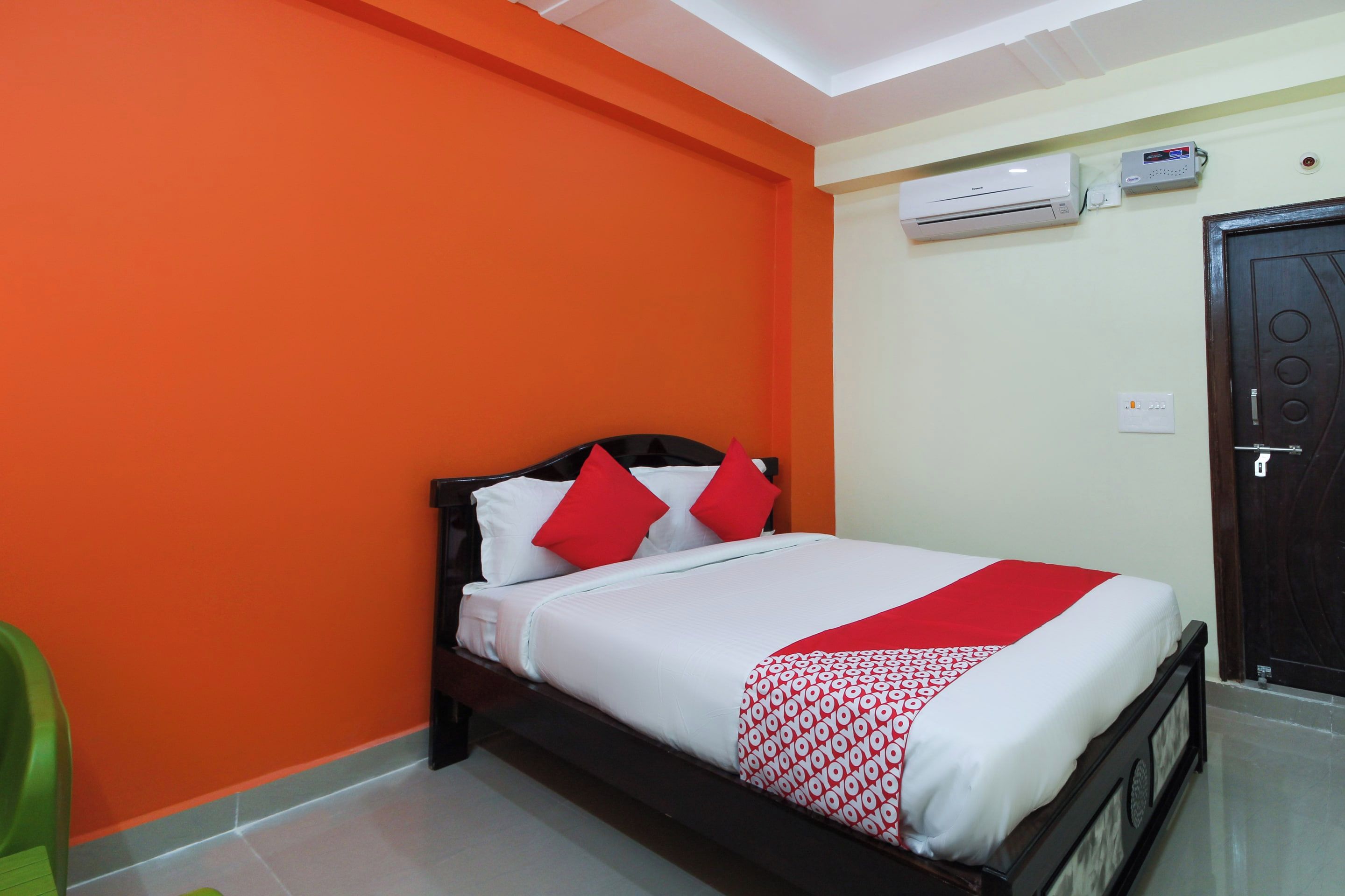 Una habitación de hotel con una cama, un equipo de aire acondicionado, una puerta y un interruptor de luz en la pared.
