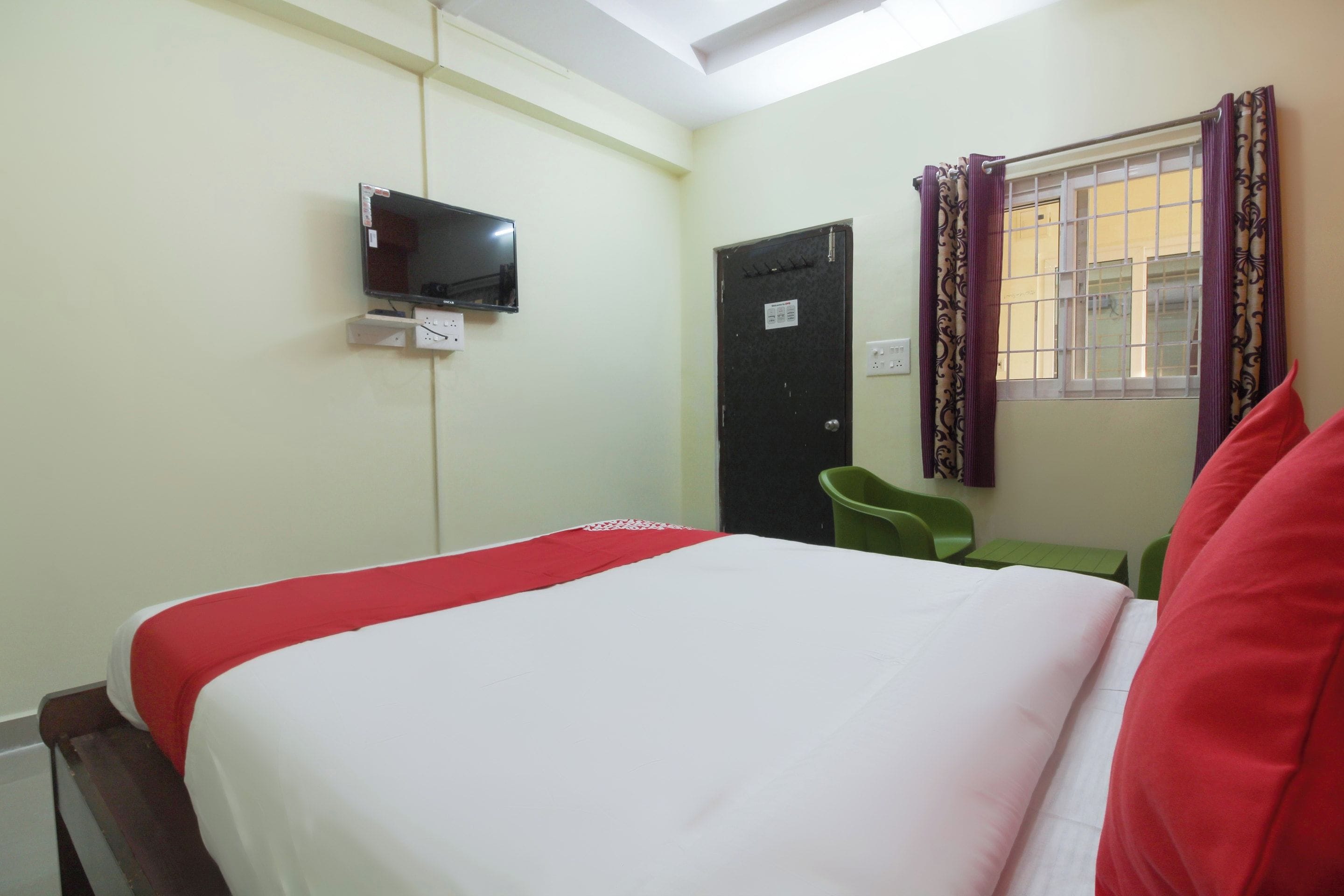 Habitación de hotel con cama, televisor en la pared, puerta y ventana con cortinas.