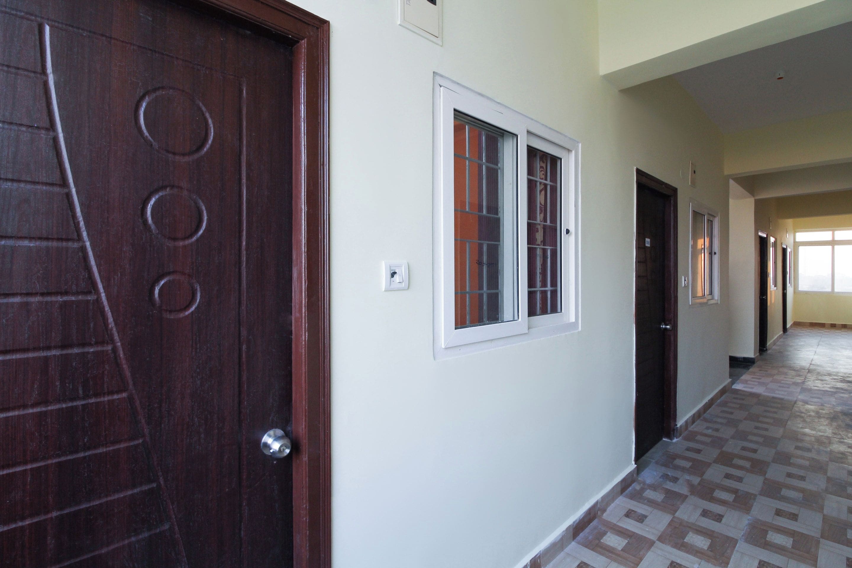A hallway with a patterned floor, a wooden door with circular designs, and a window with a white frame.