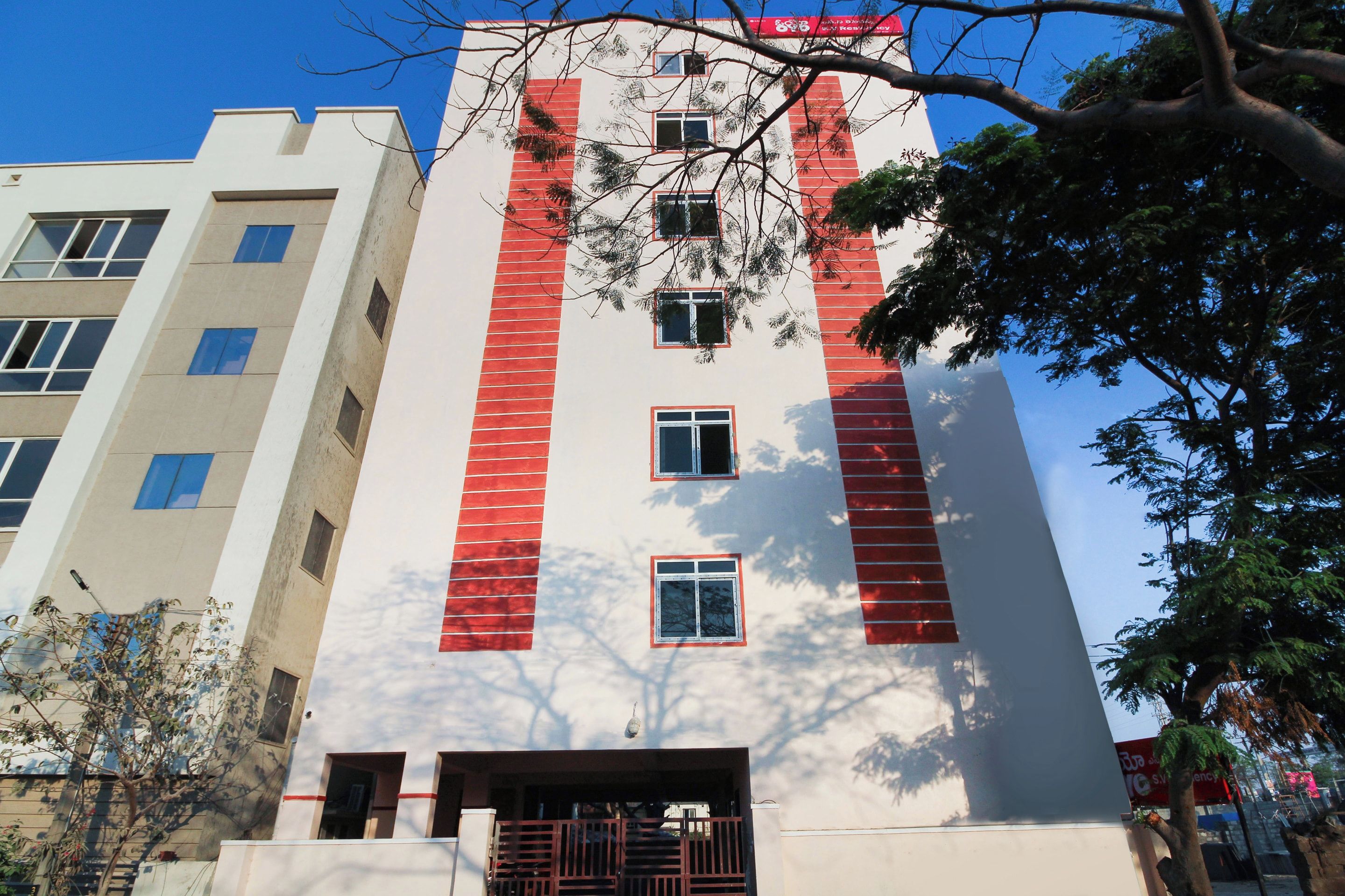 Un edificio de varios pisos con fachada blanca y detalles rojos, con múltiples ventanas y una entrada protegida por una reja.
