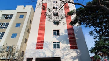 Un edificio de varios pisos con fachada blanca y detalles rojos, con múltiples ventanas y una entrada protegida por una reja.