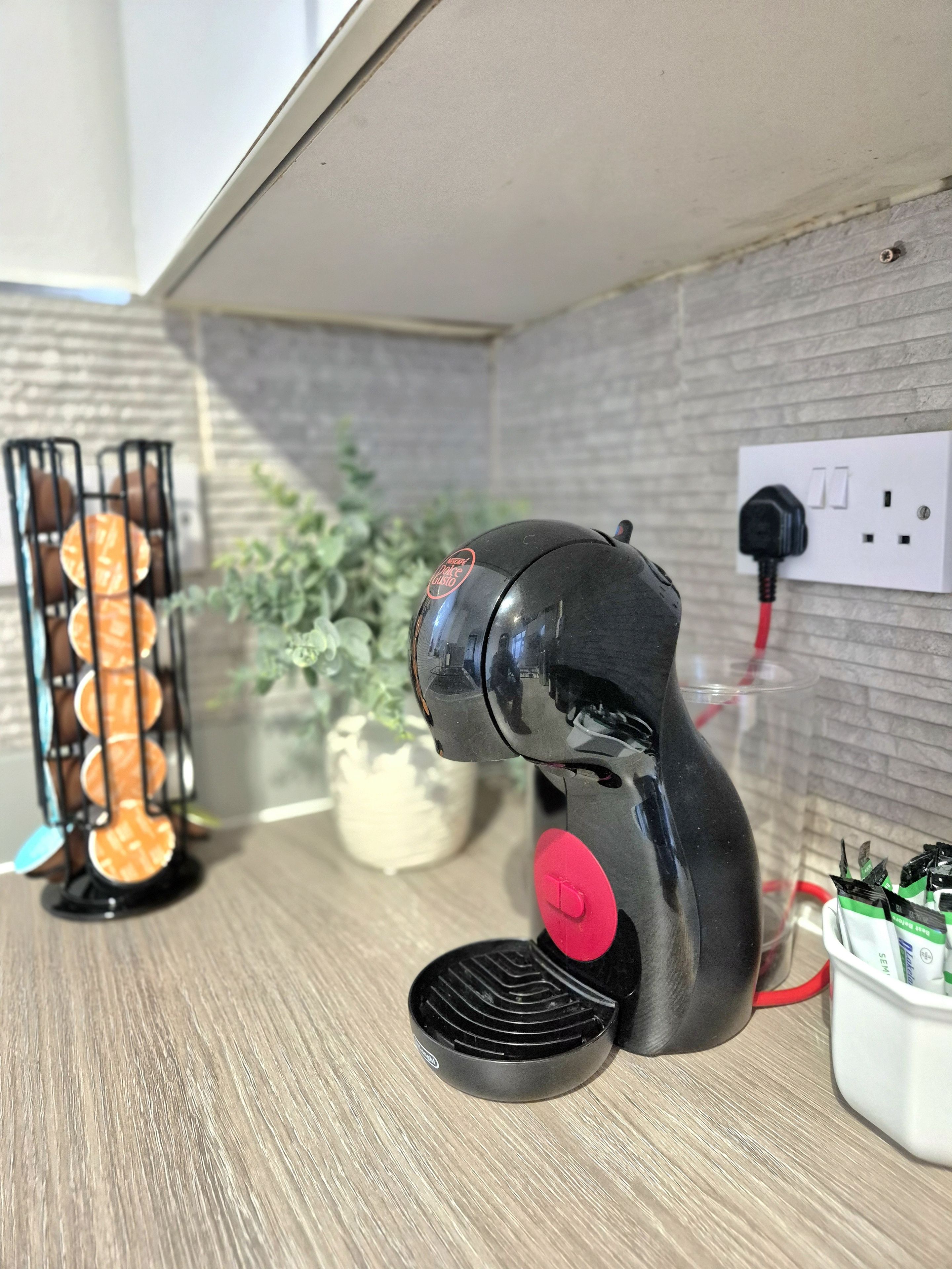 A kitchen counter with a coffee maker, a power outlet, and a plant.