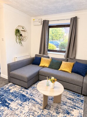 A modern living room with a grey sectional sofa, a round coffee table, and a patterned rug. - Cosy 2 Bedroom Home in Great Location (Shenley Lodge)