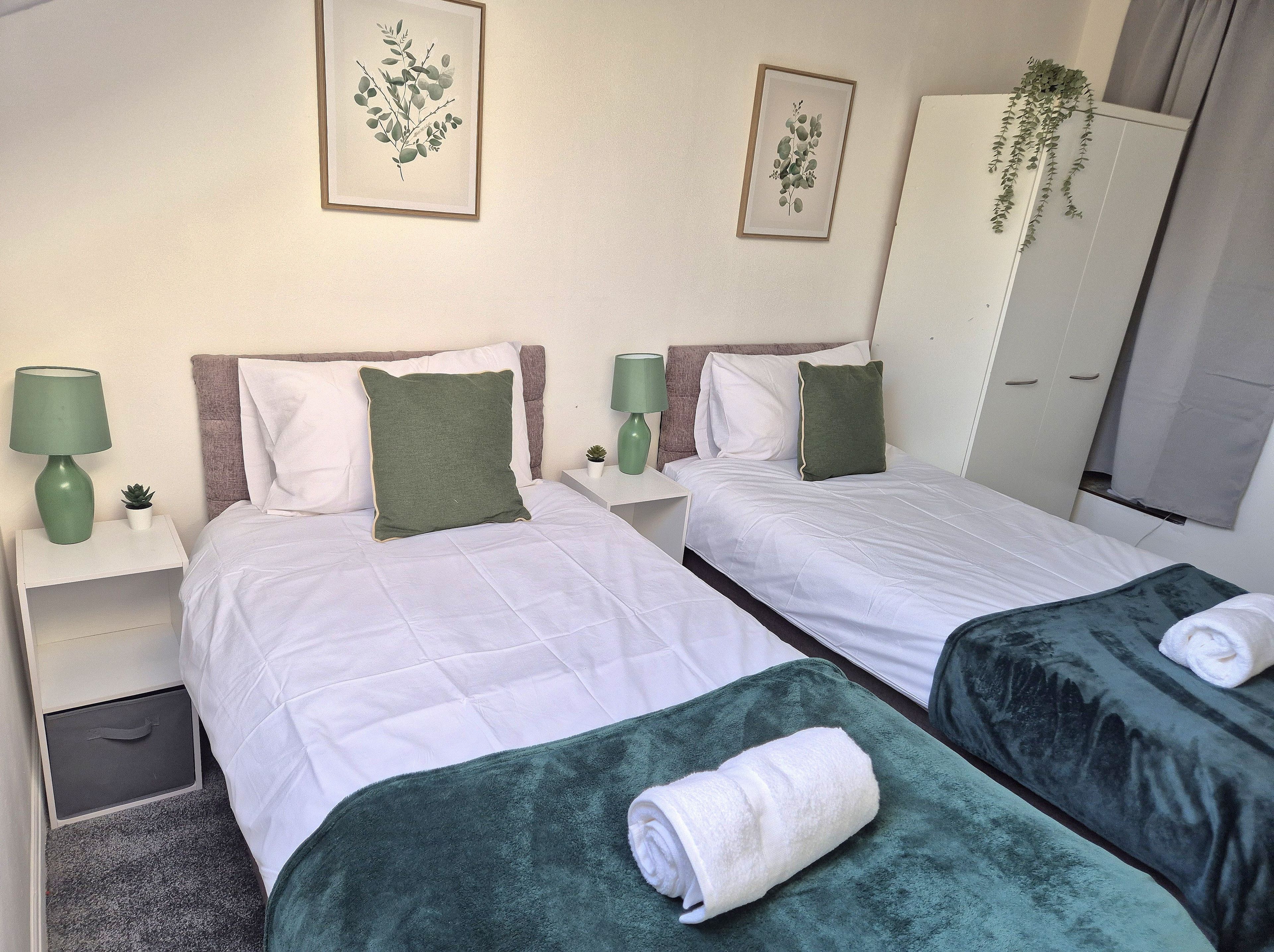 Ein Hotelzimmer mit zwei Betten, einem Kleiderschrank, einem Nachttisch mit Lampe und einer kleinen Pflanze.