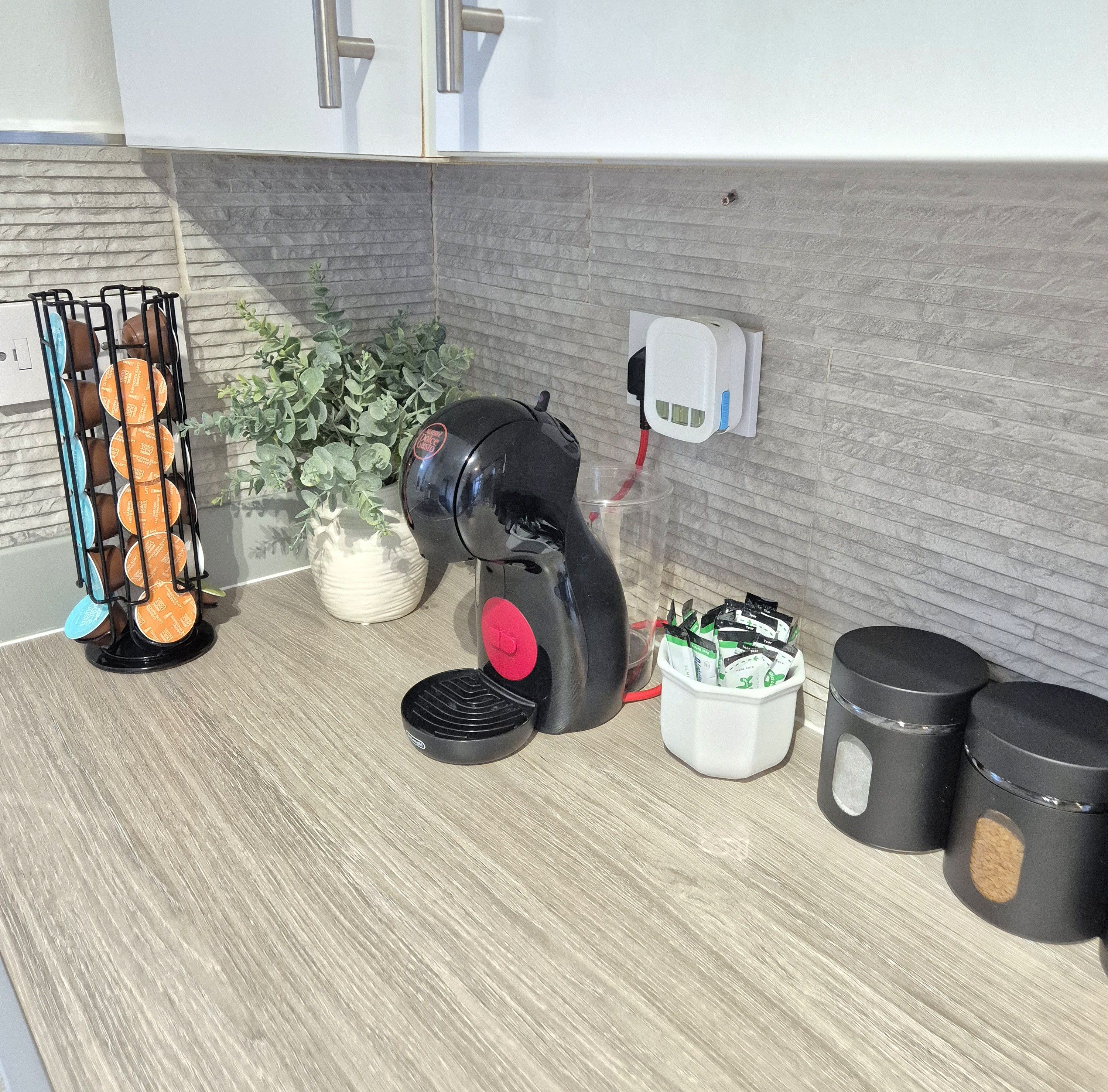 Un comptoir de cuisine avec une machine à café, une plante et un récipient contenant des capsules de café.
