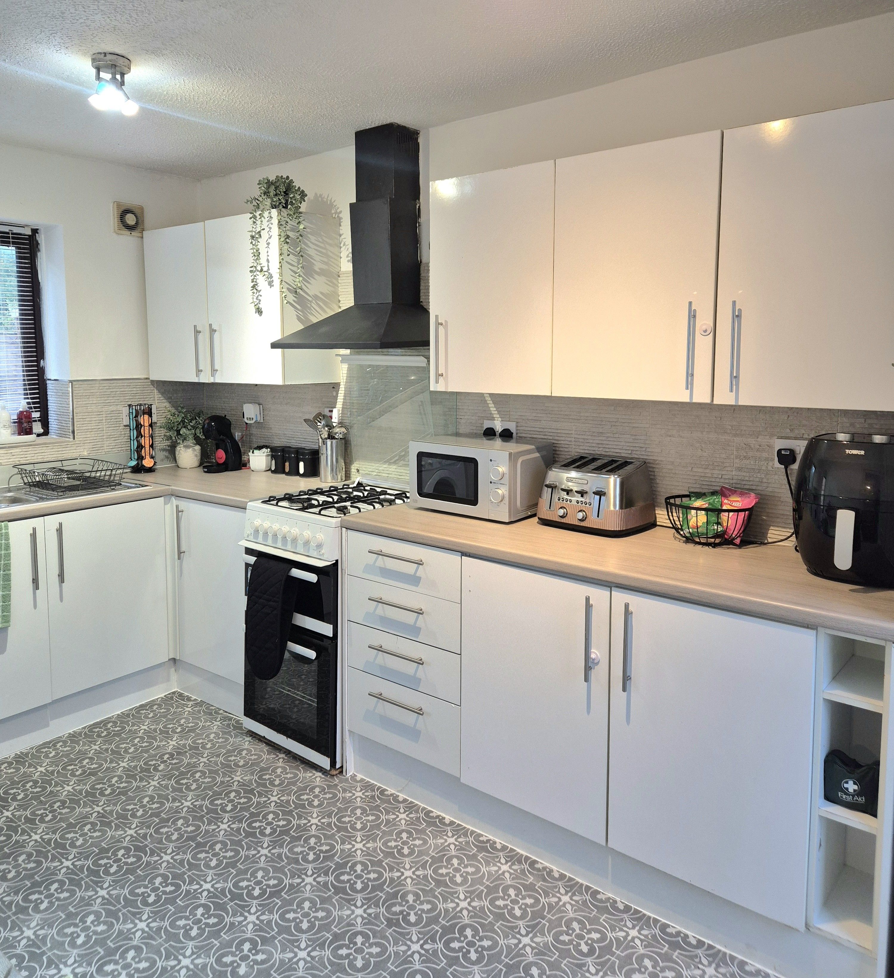 Une cuisine moderne avec des meubles blancs, une cuisinière à gaz, un four à micro-ondes et un grille-pain.