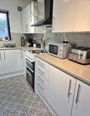 A modern kitchen with white cabinetry, a gas stove, an oven, a microwave, and a toaster. - Cosy 2 Bedroom Home in Great Location (Shenley Lodge)