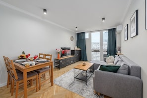 A modern living room with a dining area, a grey sofa, a TV, and a view of the city through large windows. - Lumina 2room Apart in Center I City View (Warszawa)