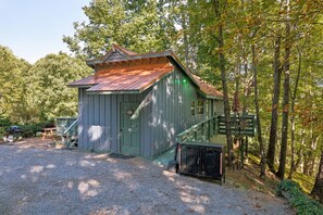 Une petite cabane à un seul étage, avec une porte verte et un toit rouge, entourée d’arbres.