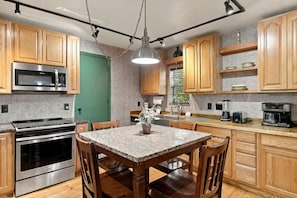 Una cocina moderna con gabinetes de madera, electrodomésticos de acero inoxidable, una encimera de granito y un comedor con mesa y sillas.